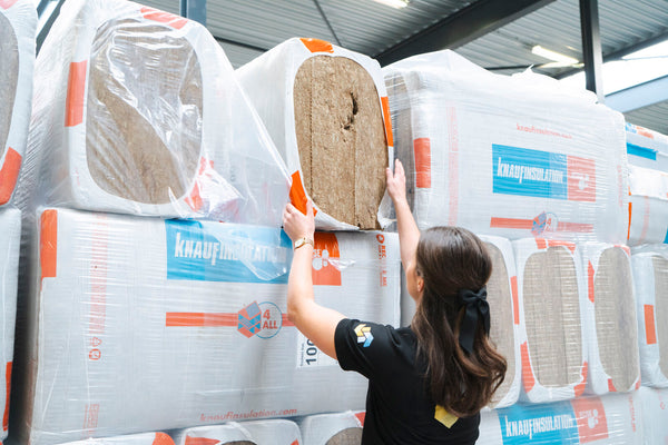 vrouw pakt pakket knauf steenwol uit magazijn